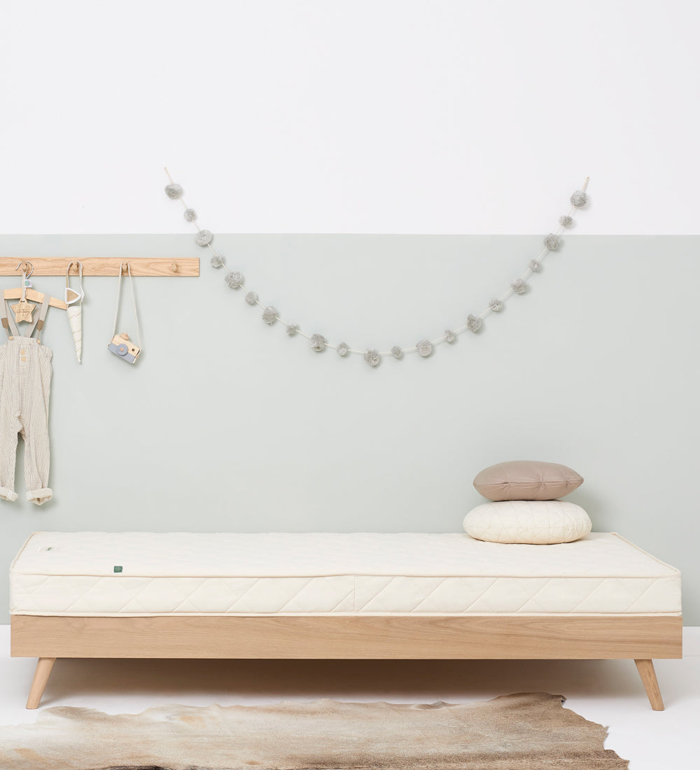 A wooden trundle bed with a Little Green Sheep atress on it. The bed is in a bedroom with walls painted white and light green.