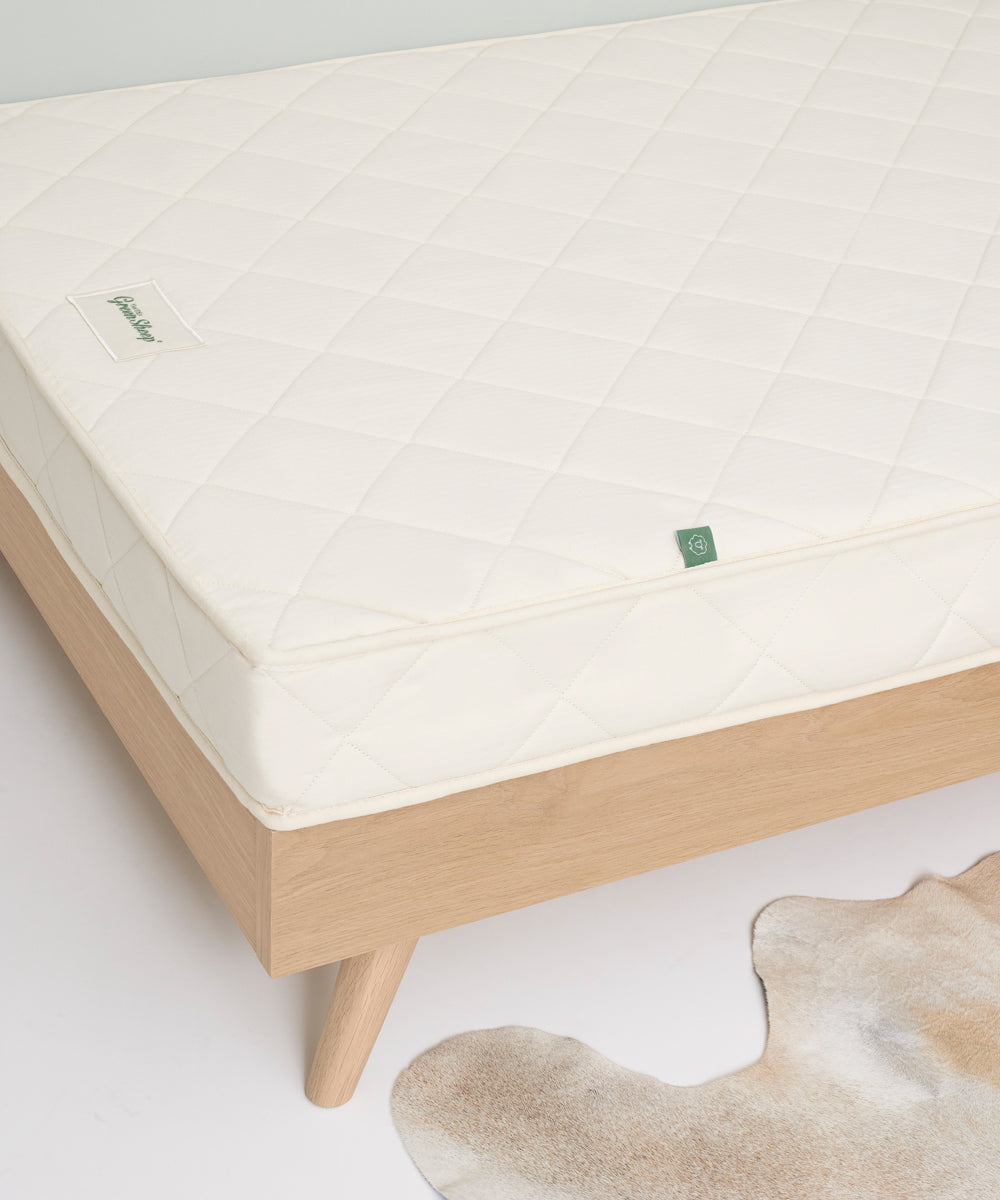 A close up of a little Green Sheep mattress on a wooden bed frame 