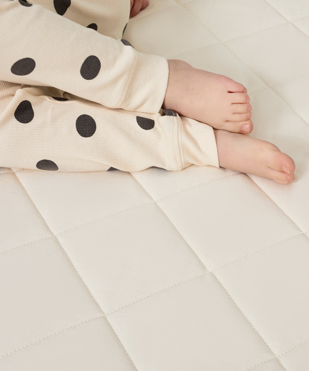 A close up of a child's feet. The child is wearing spot print pyjamas and is lying down on a Little Green Sheep mattress