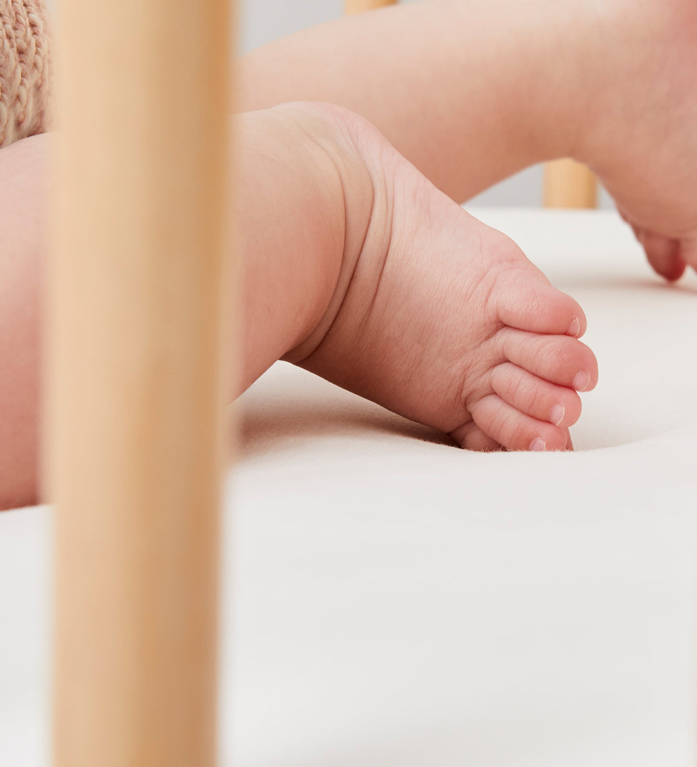 A close up of a baby's feet in a got that ha Little Green Sheep Organic Cot Jersey Fitted Sheet on it 