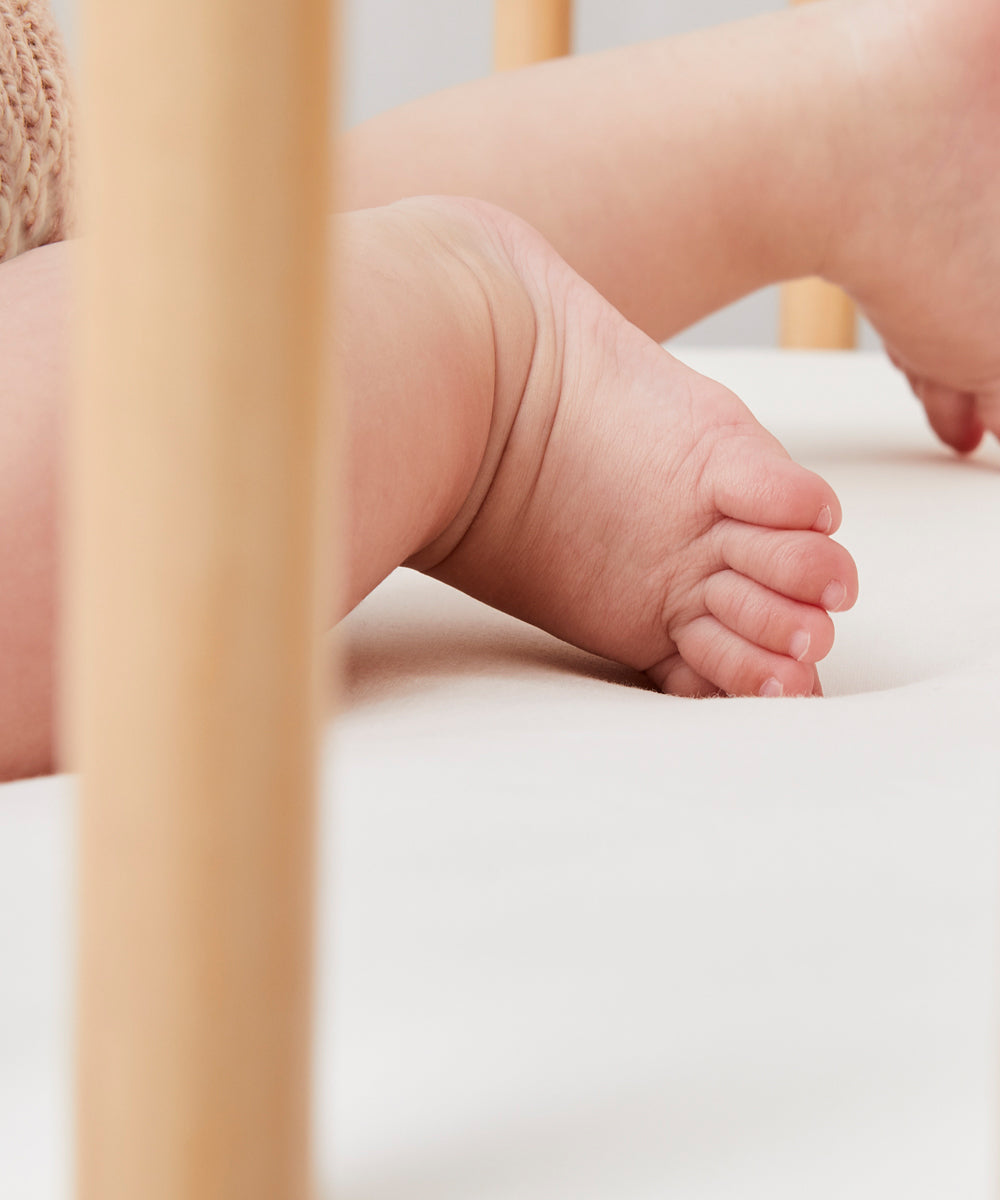 A close up of a baby's feet in a got that ha Little Green Sheep Organic Cot Jersey Fitted Sheet on it 