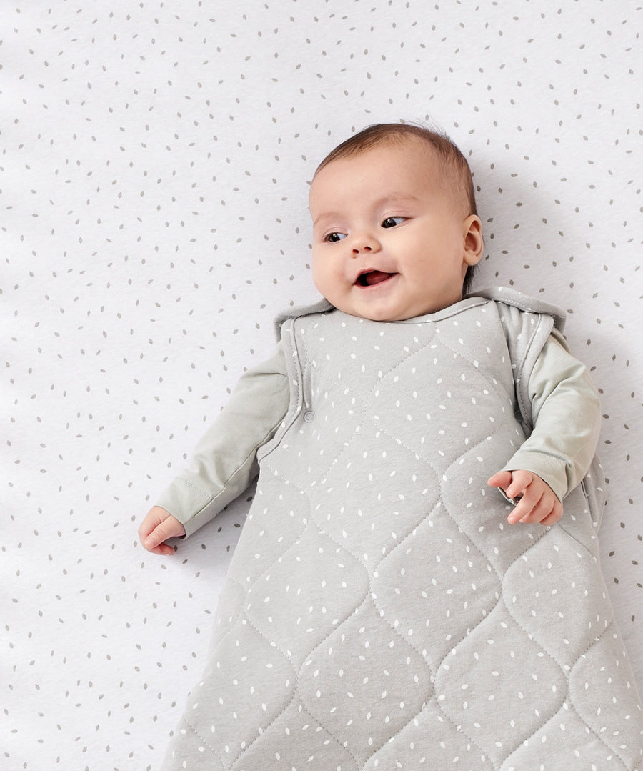 A baby lying on a rice print bed sheet wearing a dove rice print slepping bag