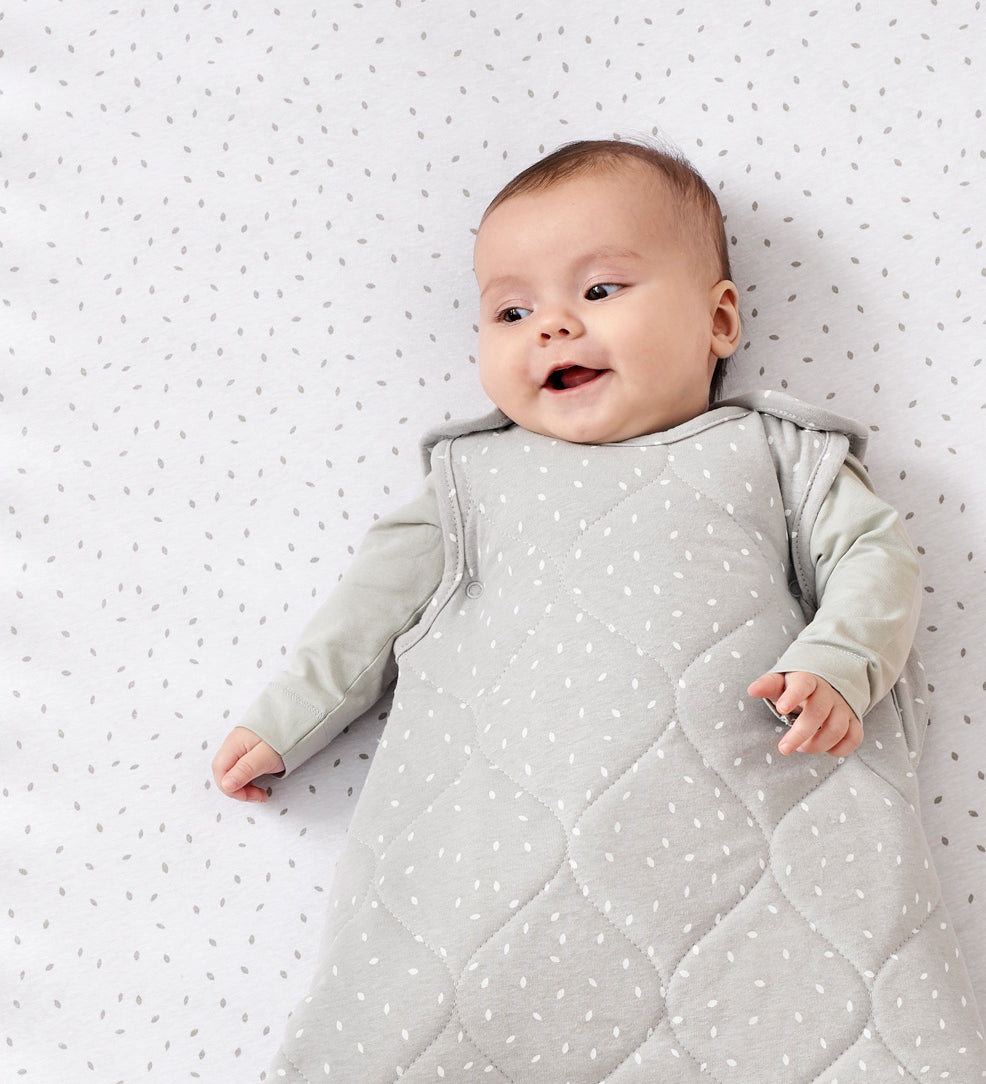 A baby lying on a rice print bed sheet wearing a dove rice print slepping bag