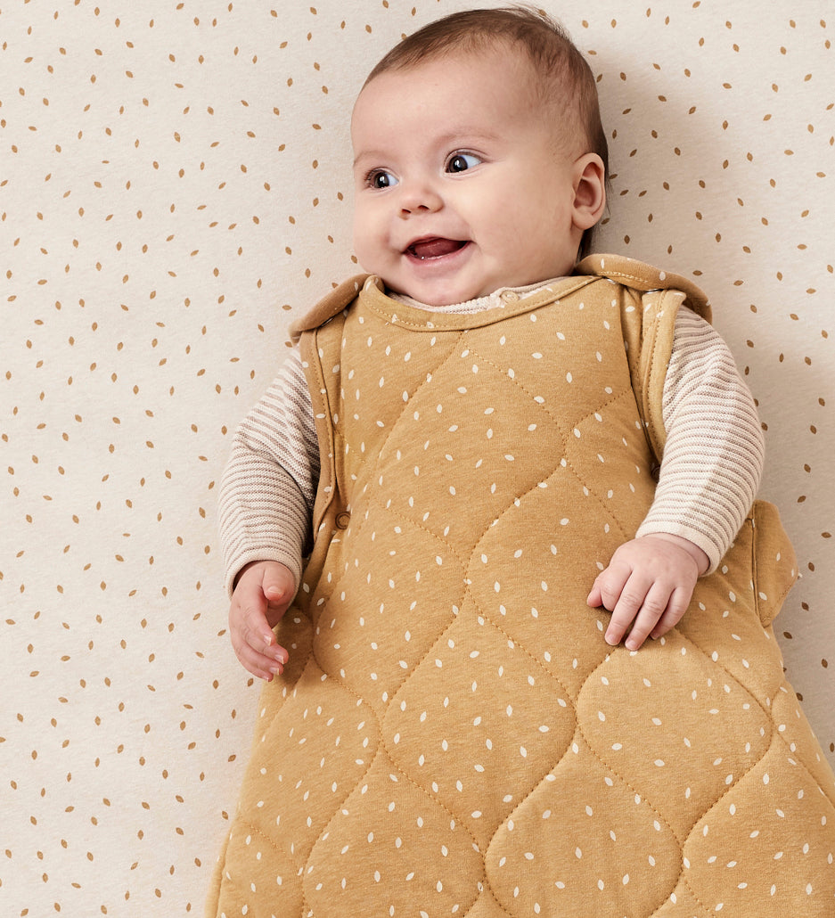 A baby ling down in a cot wearing a honey rice print Little Green Sheep baby sleeping bag