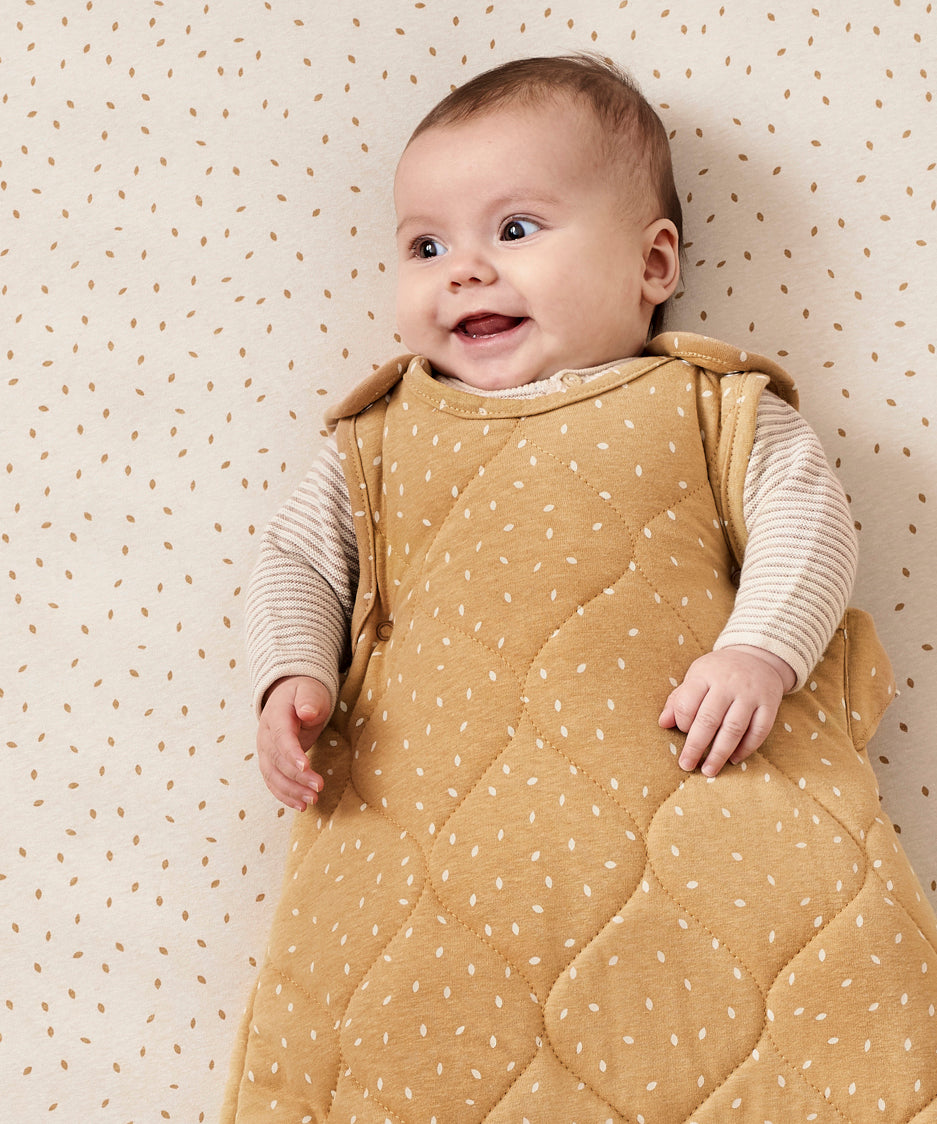 A baby ling down in a cot wearing a honey rice print Little Green Sheep baby sleeping bag