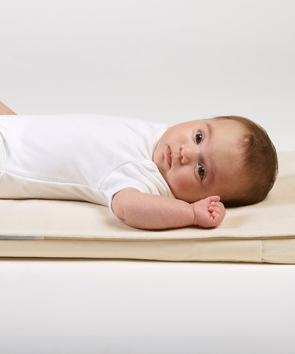 A close up of a baby lying on a Little Green Sheep Organic Moses Basket / Pram Mattress Protector