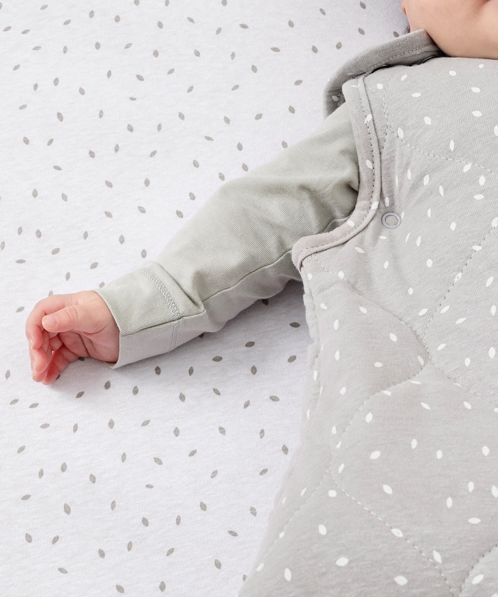 A close up of the popper closure underneath the baby's arm on the dove rice print 2.5 tog baby sleeping bag