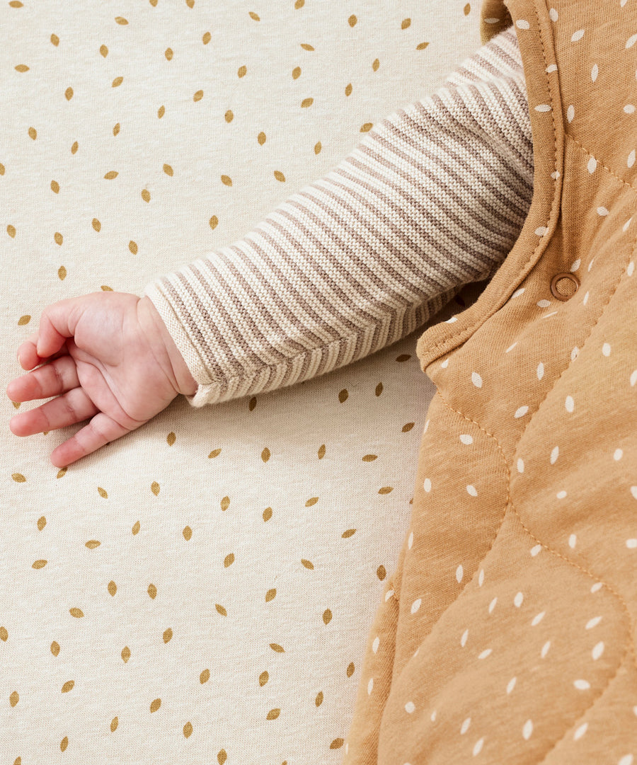 A close up of the popper closure detail underneath a baby's arm on the Little Green Sheep Organic Baby Sleeping Bag 2.5 Tog in Honey Rice print