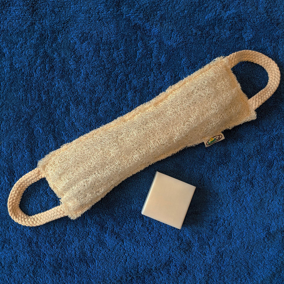 LoofCo Loofah Back Scrubber pictured alongside a soap bar on a blue towel