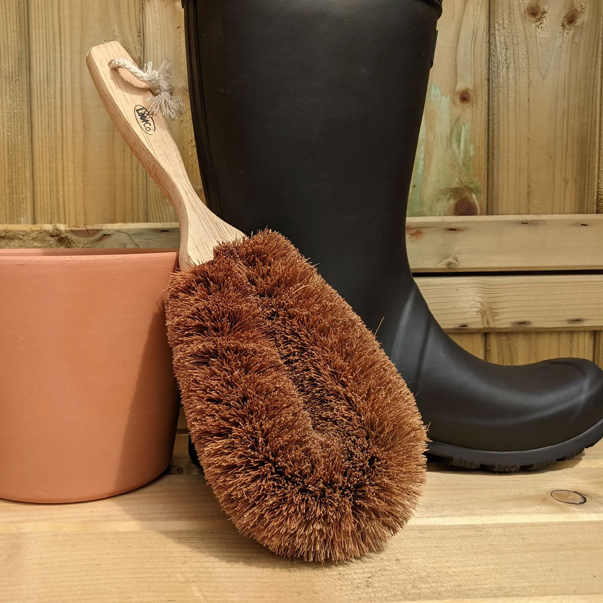 LoofCo Gardener's coconut coir garden Brush pictured placed in front of a black wellington boot and terracotta garden pot