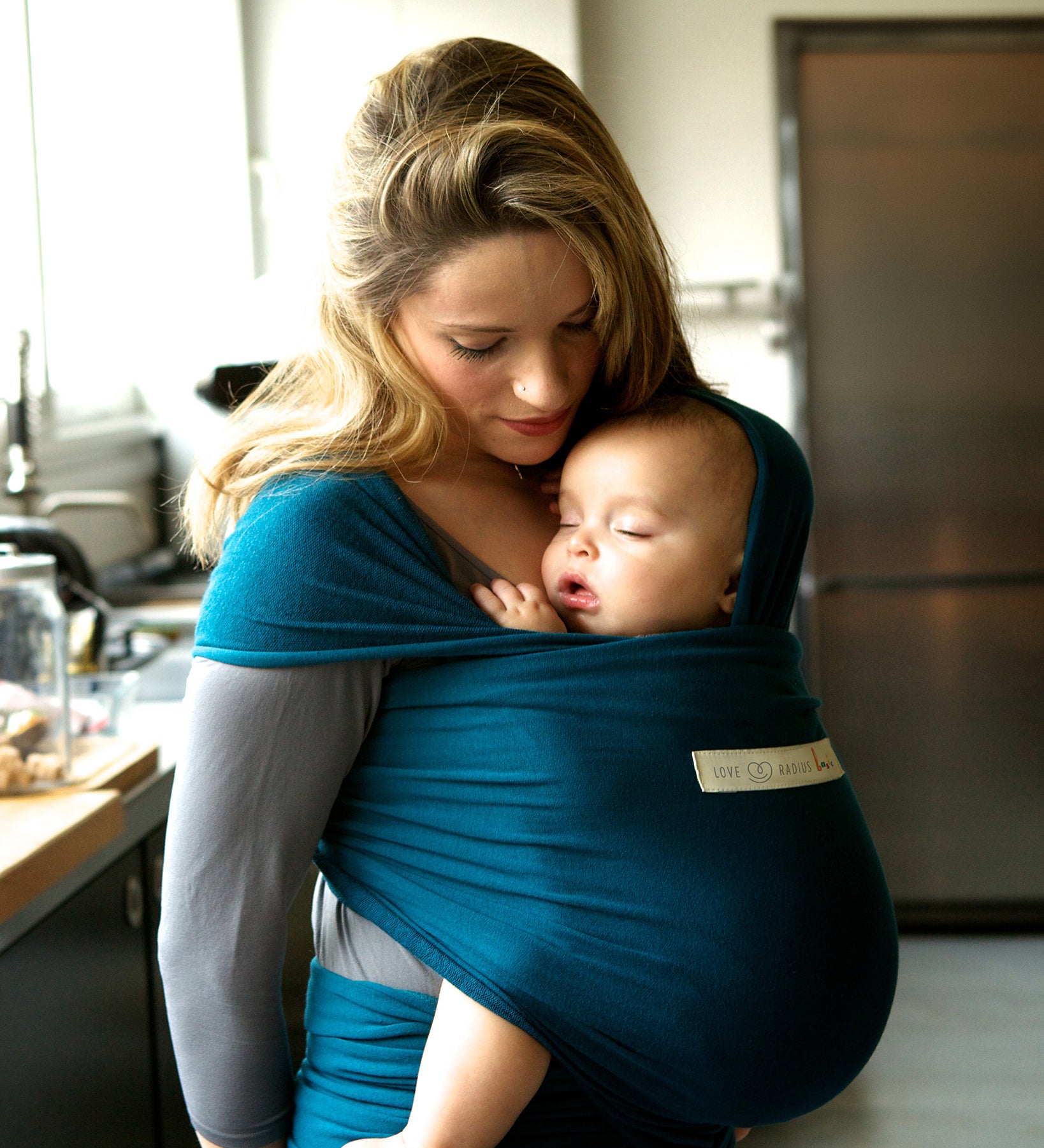 Adult carrying a baby in the Love Radius Organic Baby Wrap in Retro Blue. 