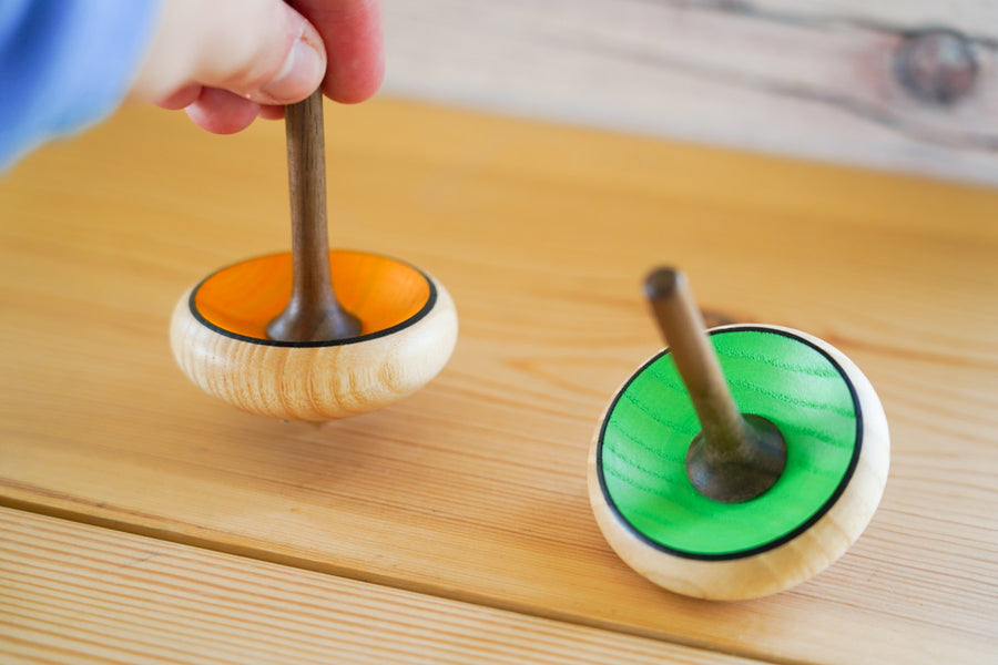 Close up of a hand holding the Mader hand carved Zwirbel spinning top on a wooden worktop