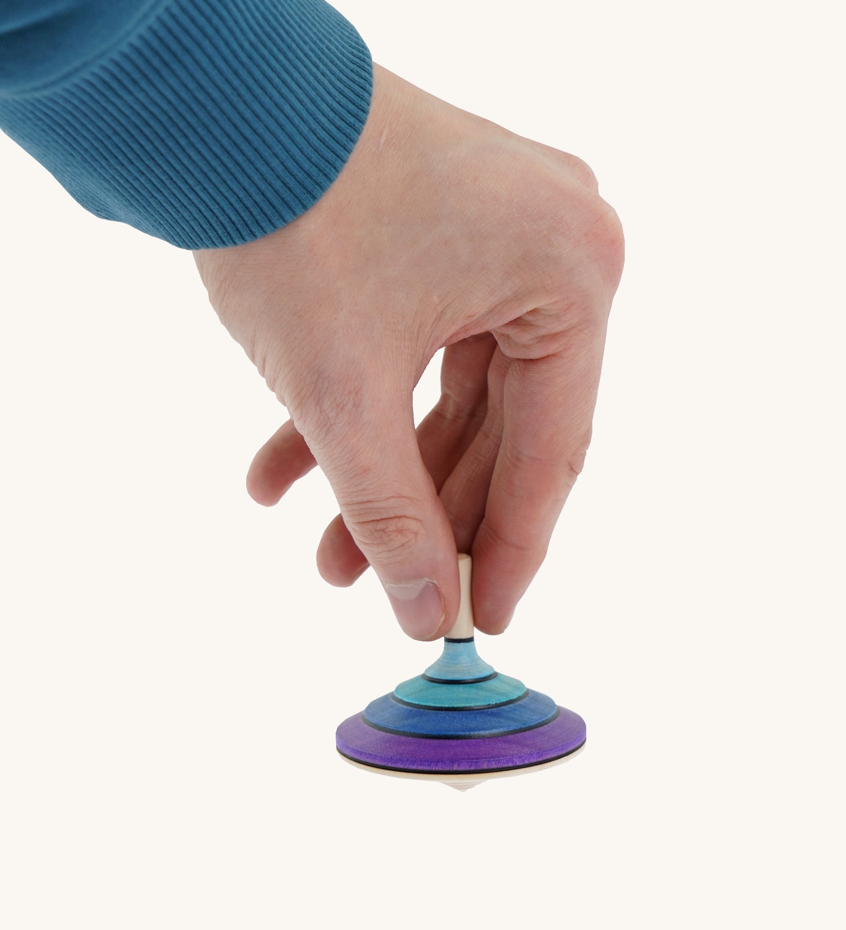 A wooden purple and blue flamenco Mader spinning top held by a hand on a cream background.