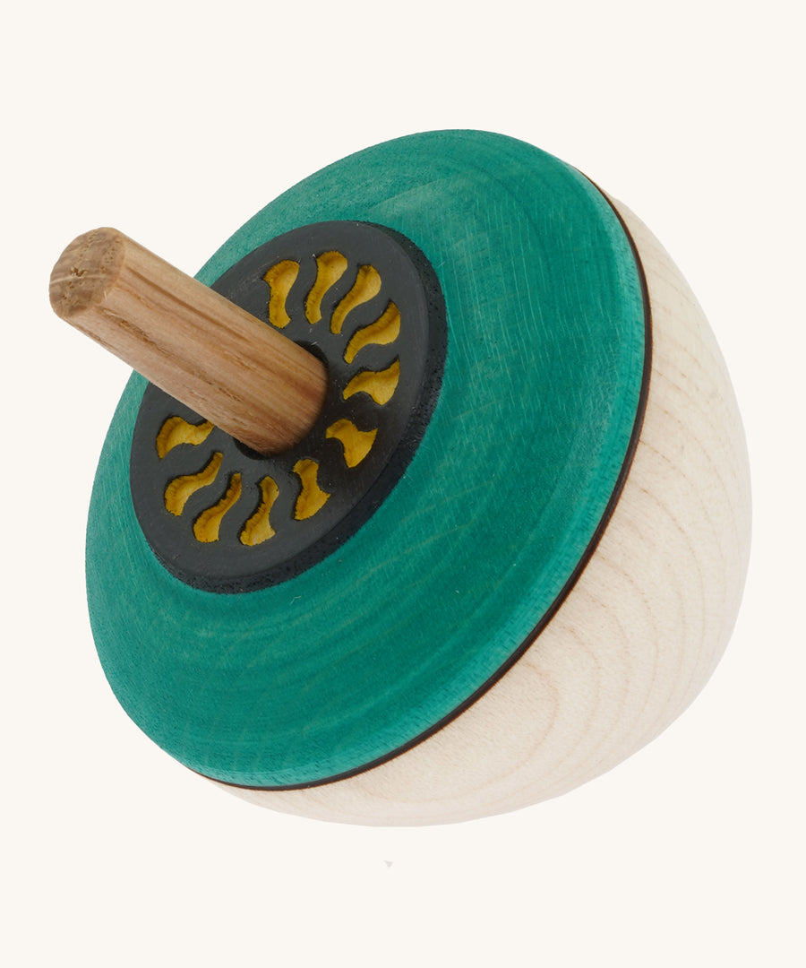 A wooden flower egg Mader spinning top with a green painted and  a yellow cut out design on the top on a cream background.