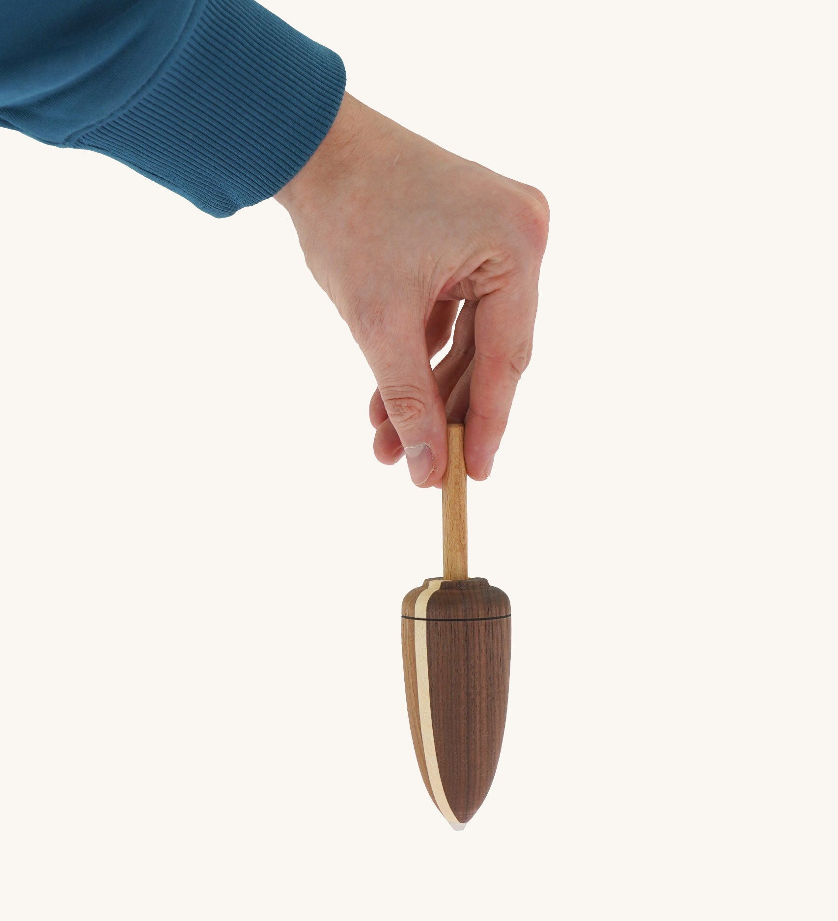 A wooden Mader goliath spinning top held by a hand on a cream background.