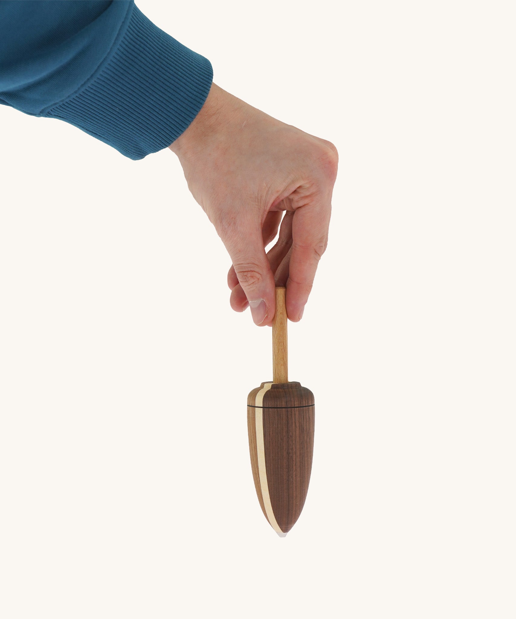 A wooden Mader goliath spinning top held by a hand on a cream background.