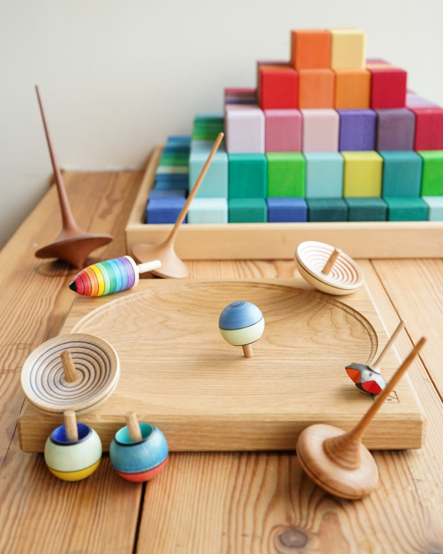 Mader wooden spinning tops on a Mader spinning plate next to a Grimms Large Stepped Pyramid