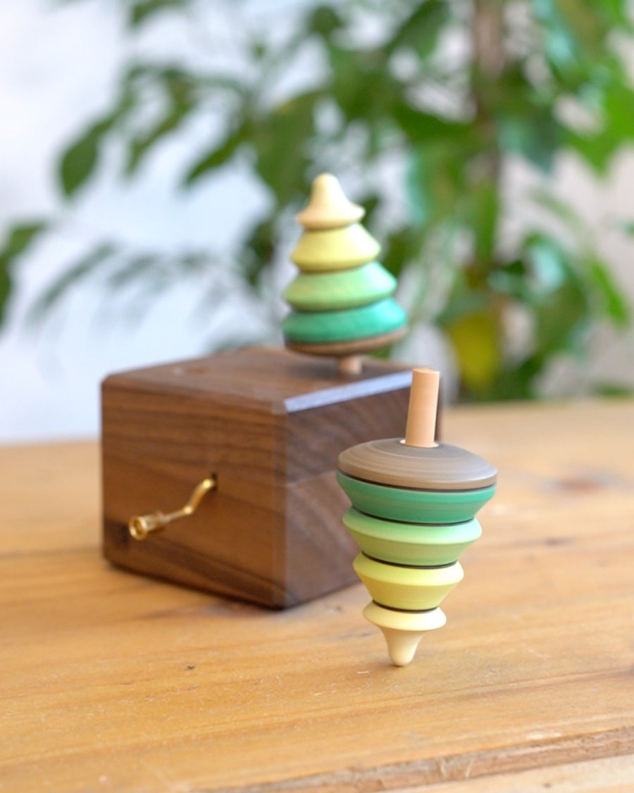 Close up of a Mader spinning top spinning next to a Mader wooden music box