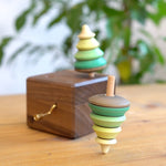 Close up of a Mader spinning top spinning next to a Mader wooden music box