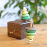 Close up of a Mader spinning top spinning next to a Mader wooden music box