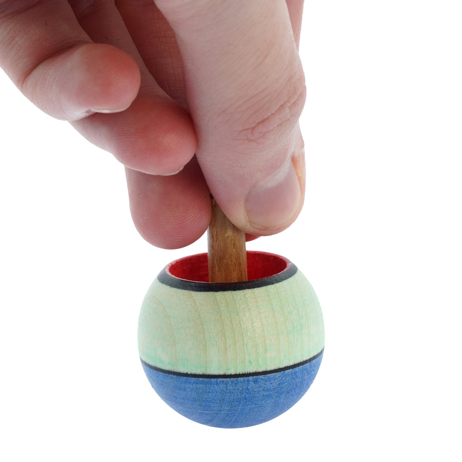 Close up of a hand holding the Mader hand carved wooden confetti turn over spinning top on a white background