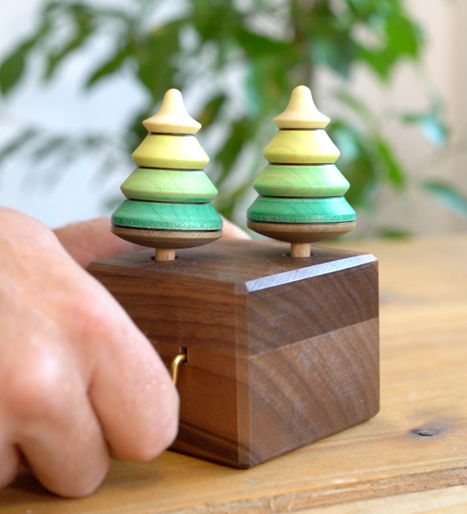 Close up of a hand turning the Mader wooden music box on a wooden table