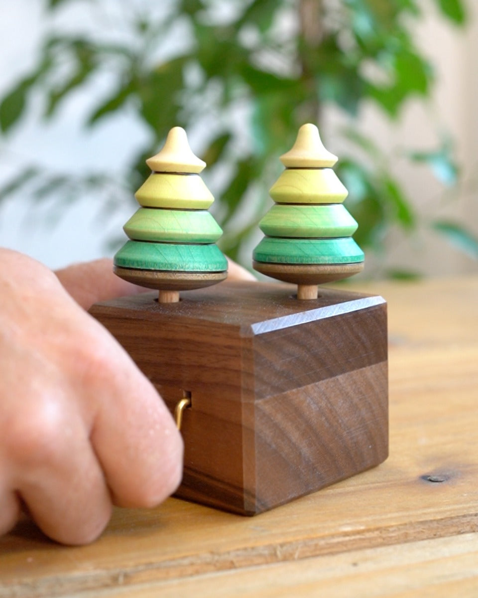 Close up of a hand turning the Mader wooden music box on a wooden table