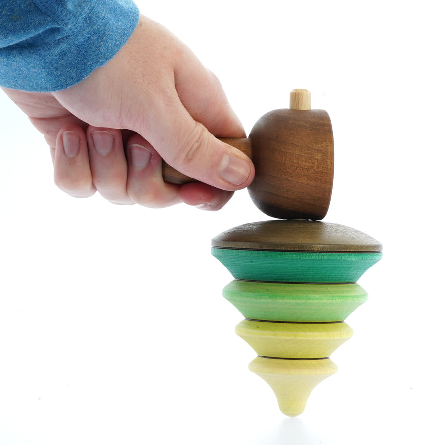 Close up of a hand holding the Mader hand carved pull string tree spinning top toy on a white background