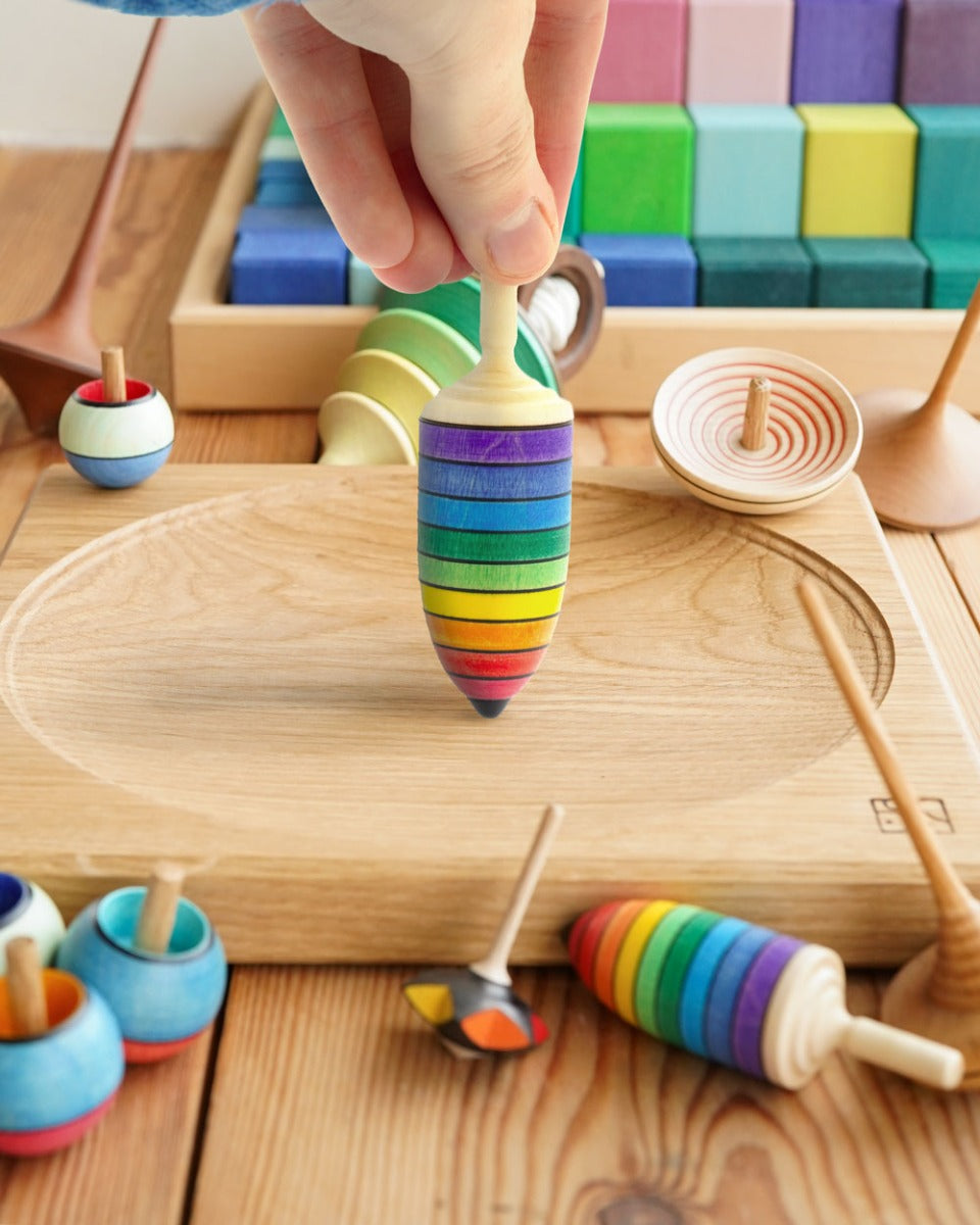 Close up of hand holding the Mader rainbow thunderbolt spinning top toy on a Mader spinning plate