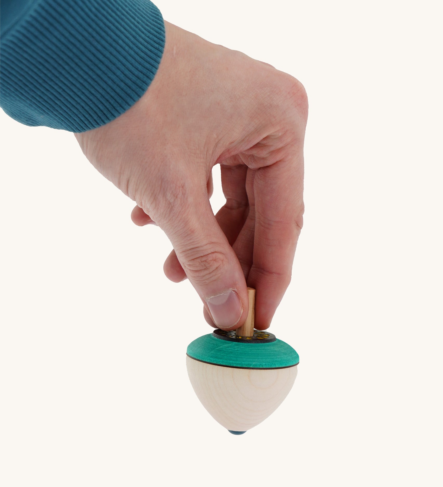 A wooden flower egg Mader spinning top held by a hand on a cream background.