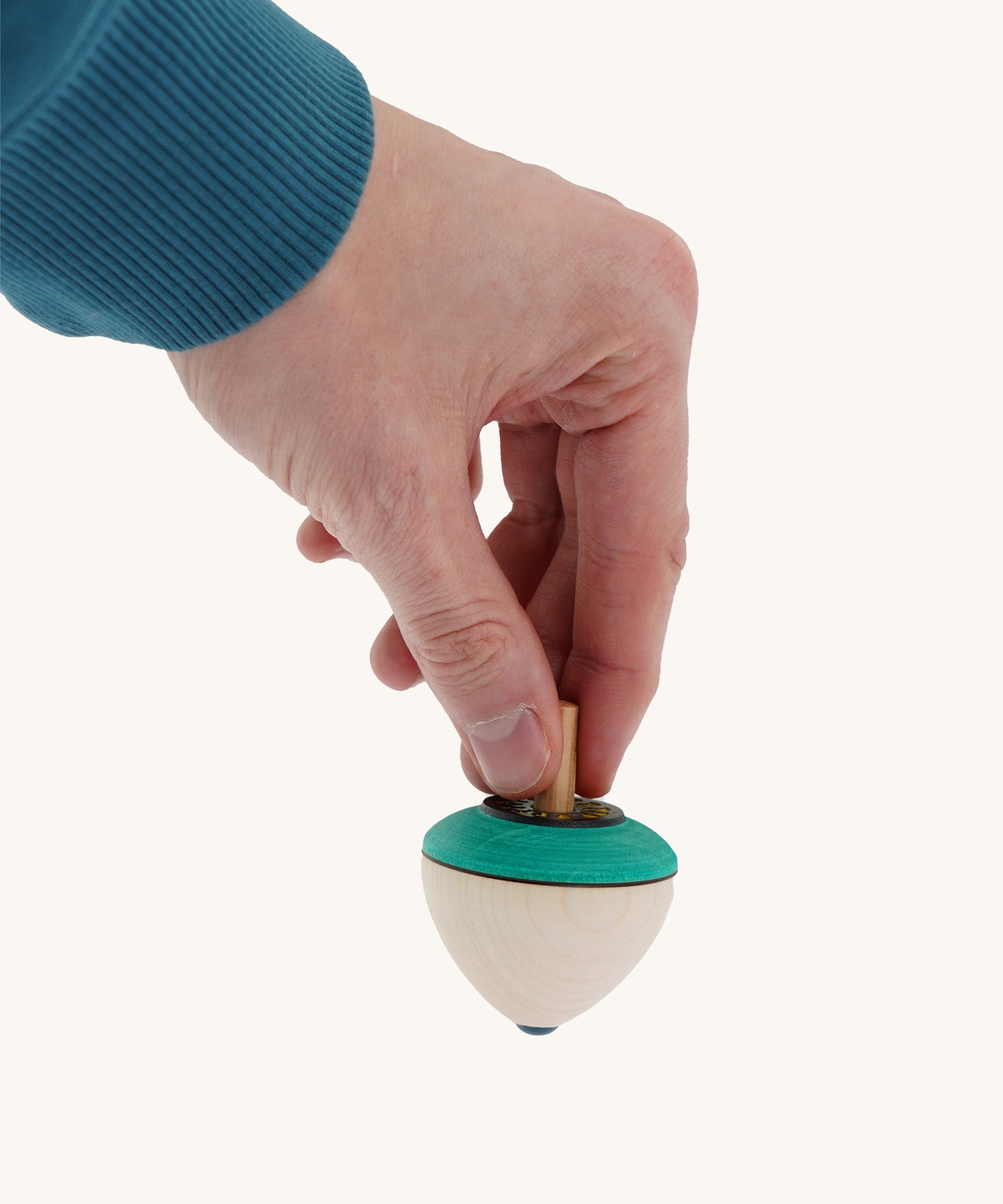 A wooden flower egg Mader spinning top held by a hand on a cream background.