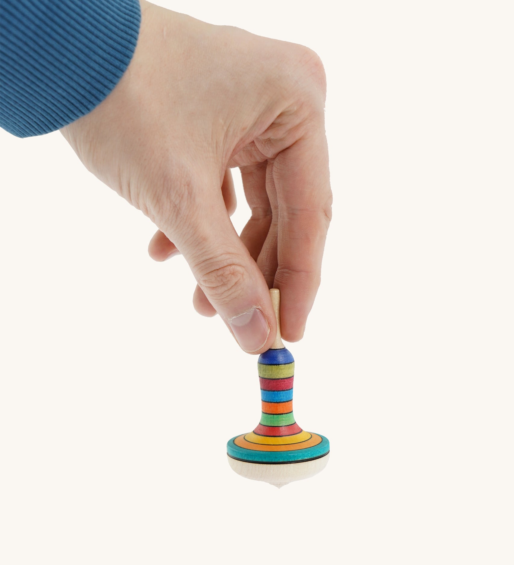 A wooden manolette spinning top held by a hand on a cream background.