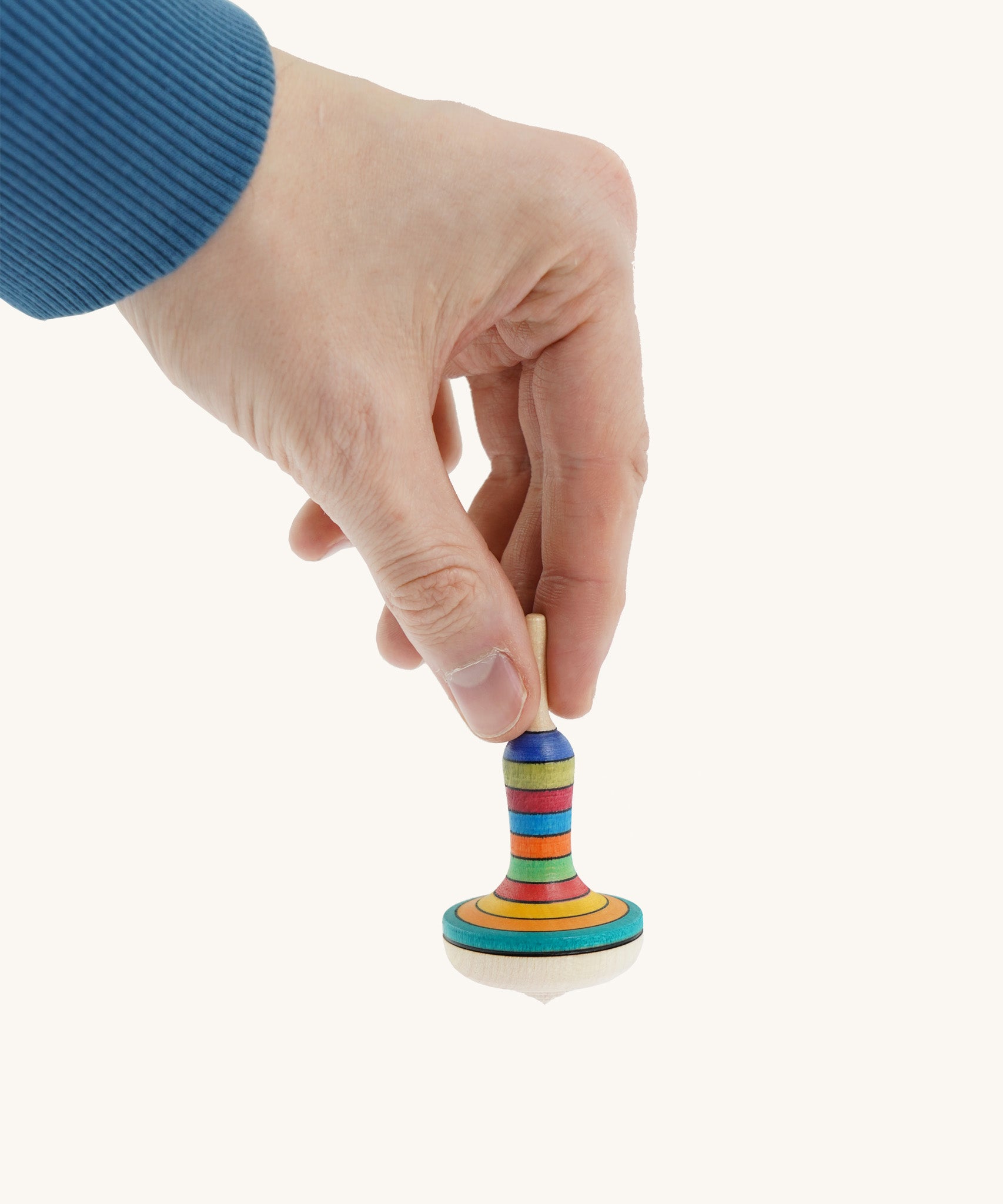 A wooden manolette spinning top held by a hand on a cream background.