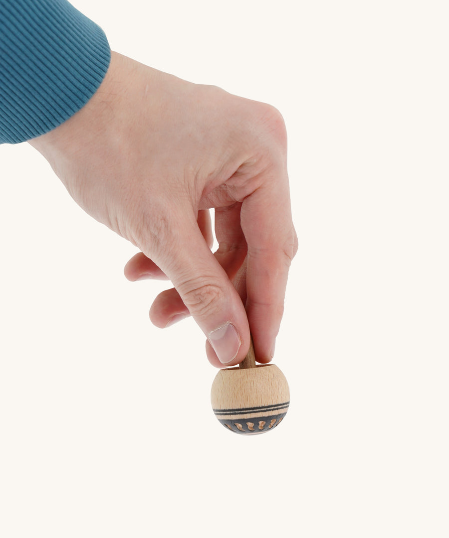 A wooden Mader Oriental spinning top held by a hand on a cream background.