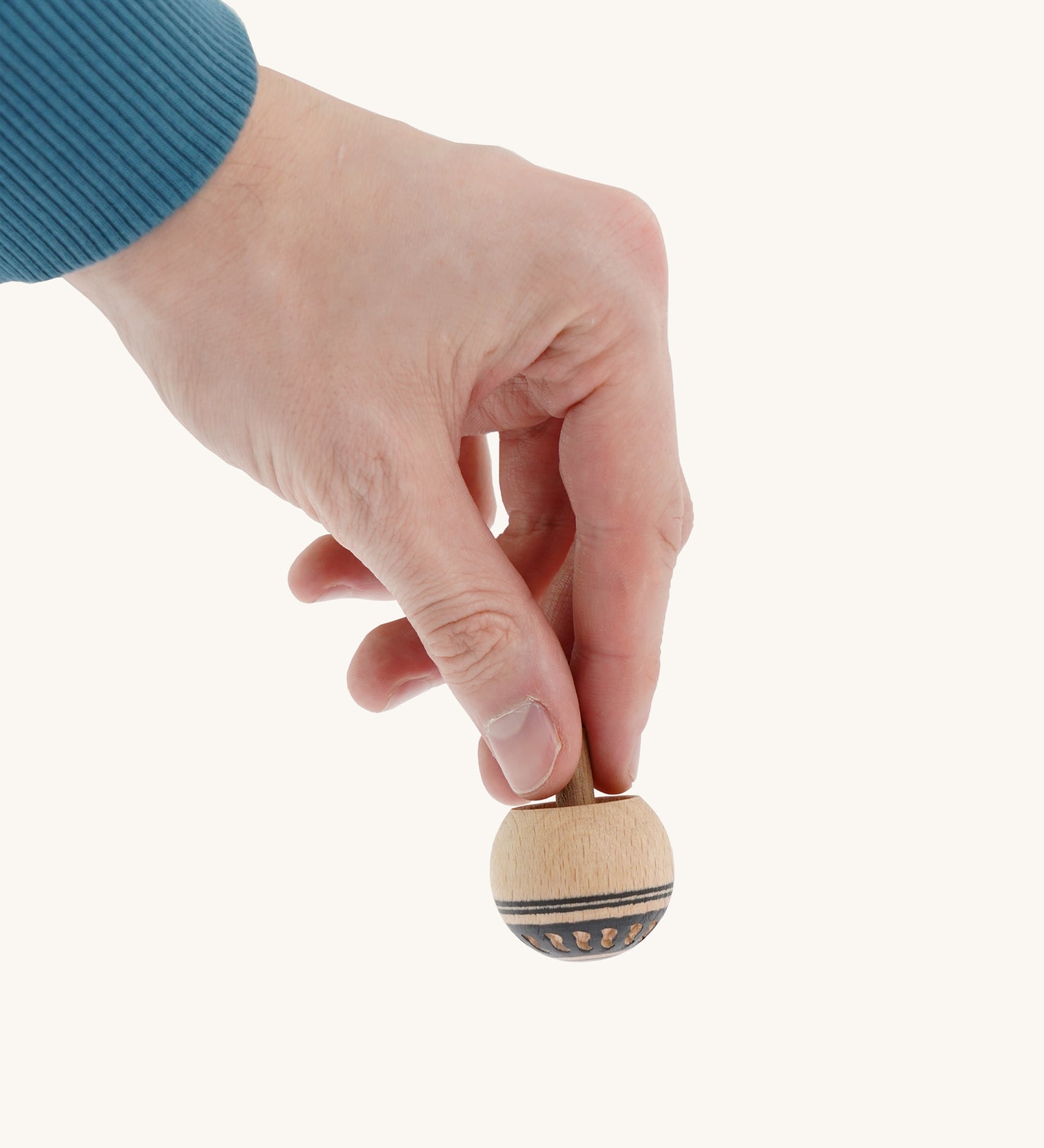 A wooden Mader Oriental spinning top held by a hand on a cream background.