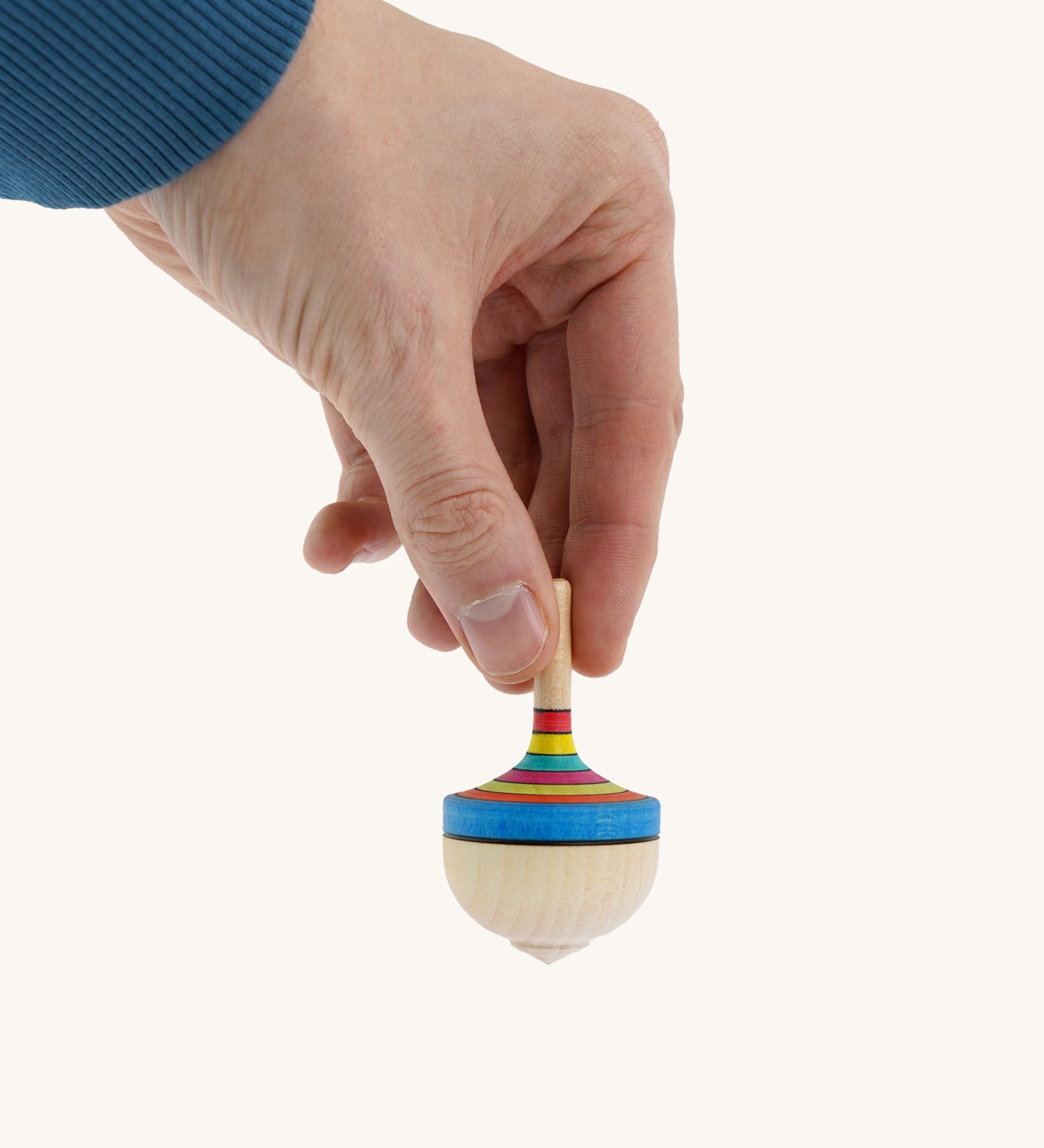 A wooden Mader traditional rainbow spinning top held by a hand on a cream background.