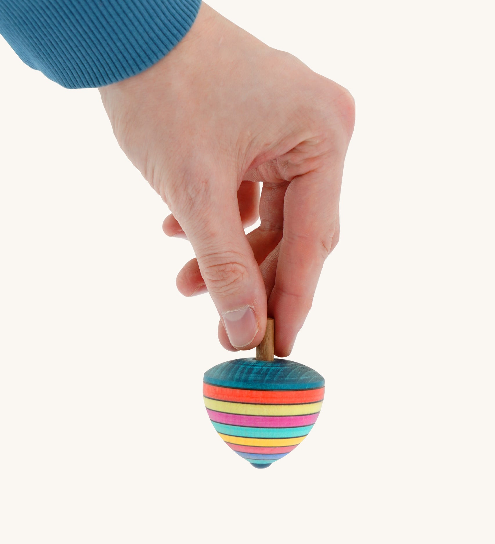 A wooden Mader dragon egg spinning top with multicoloured stripes  held by a hand on a cream background