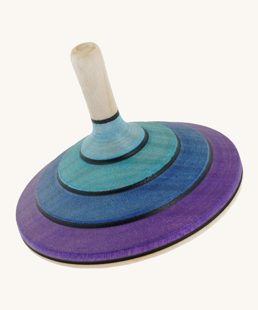 A wooden purple and blue flamenco Mader spinning top on a cream background.