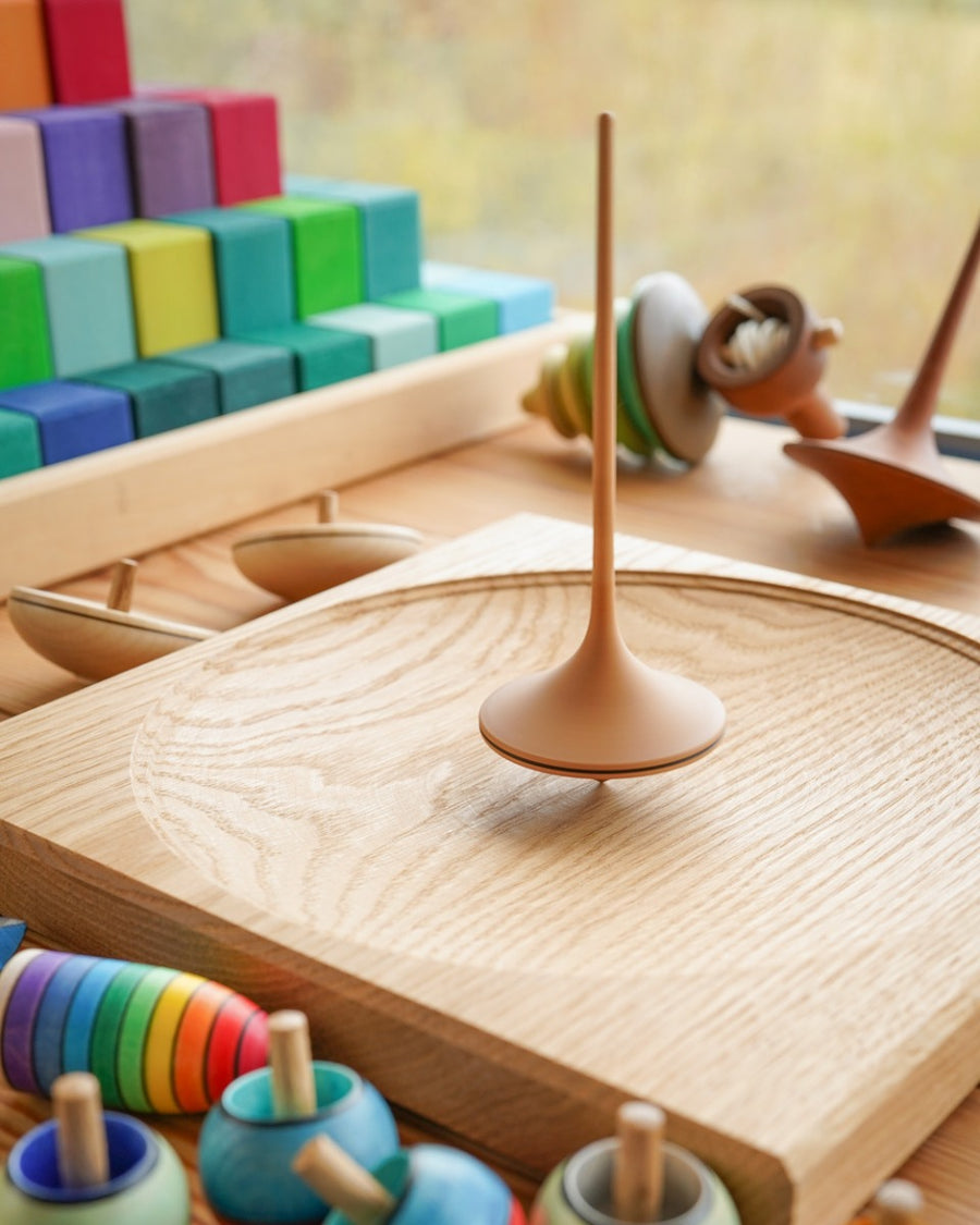 Mader wooden Trumpo spinning top on a Mader spinning plate surrounded by wooden spinning tops and a Grimms Large Stepped Pyramid