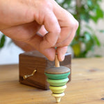 Close up of a hand holding the spinning top from the Mader wooden music box on a wooden table