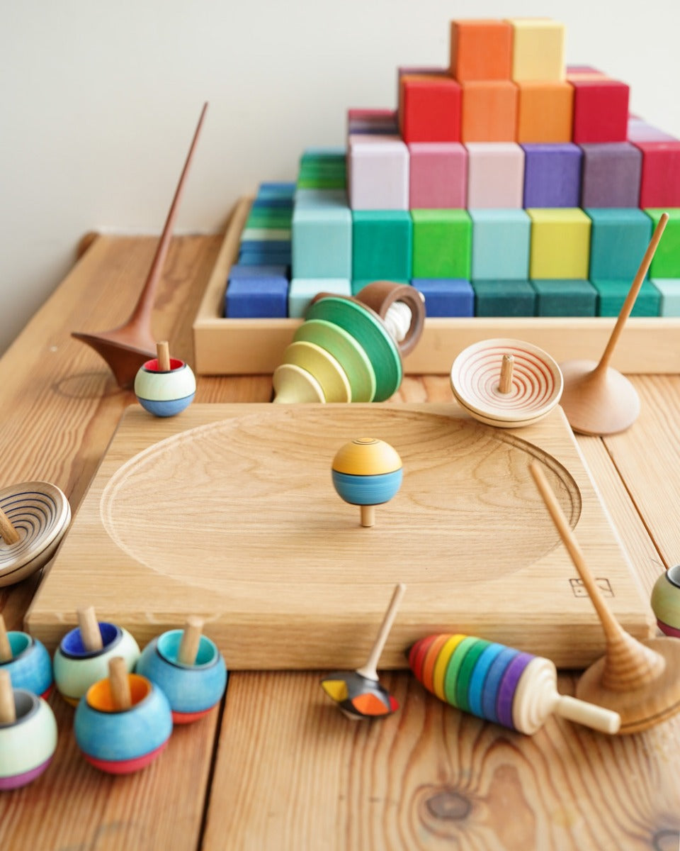 Mader wooden spinning top collection laid out next to a Mader spinning plate and a Grimms Large Stepped Pyramid