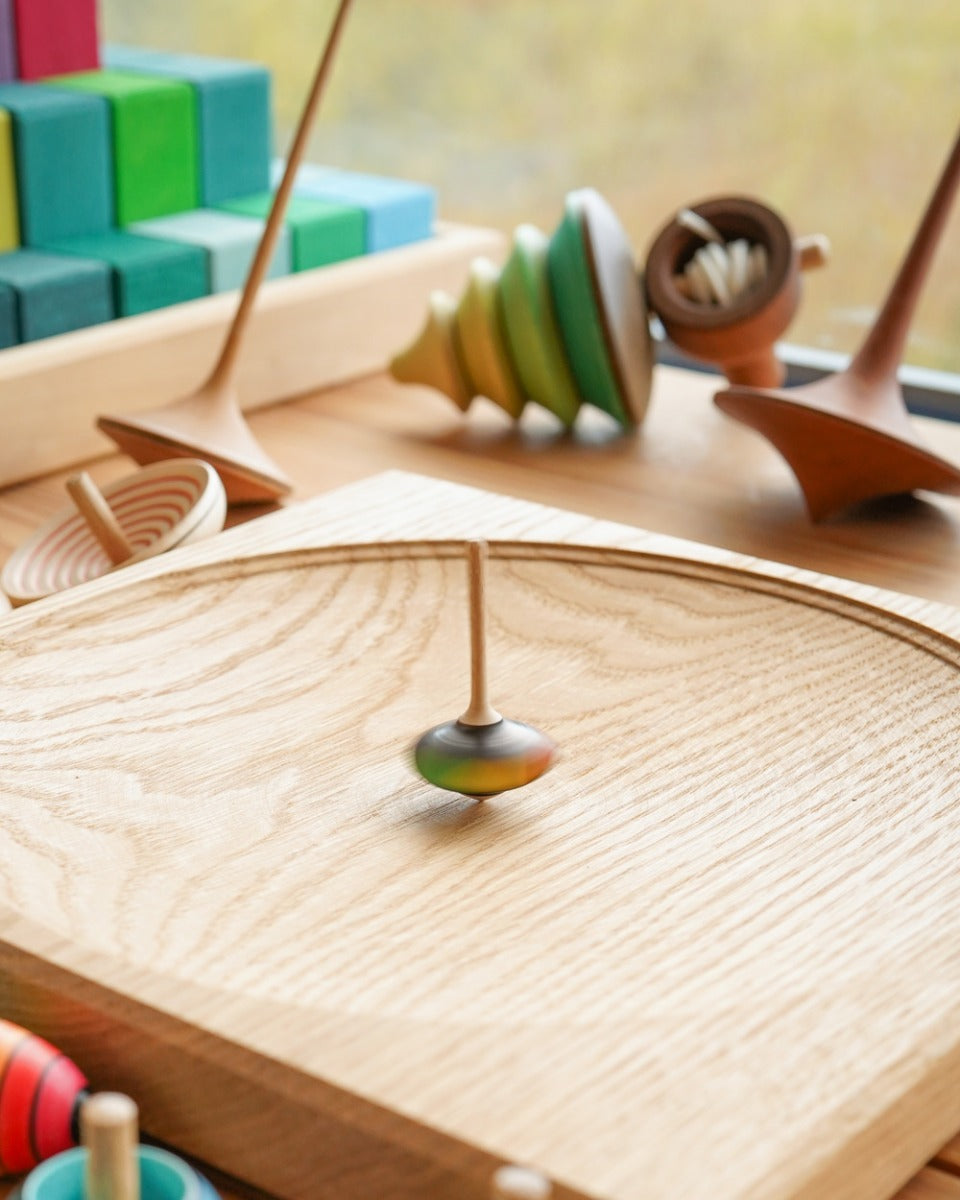 Close up of the Mader mini superstar spinning top on a Mader spinning plate next to some wooden spinning tops