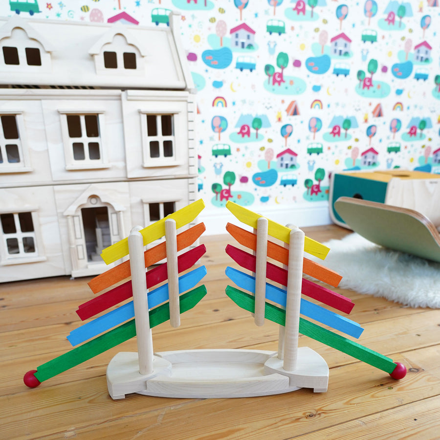 Magic Wood Reverse Ball Run pictured on a wooden floor of a playroom. A Plan Toys wooden dolls house and a Wobbel board can be seen in the background