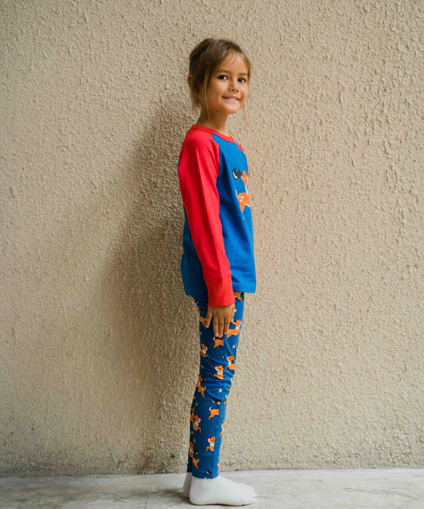 A side view of a child wearing a Maxomorra Reindeer Raglan Long Sleeve Top with reindeer print leggings. 