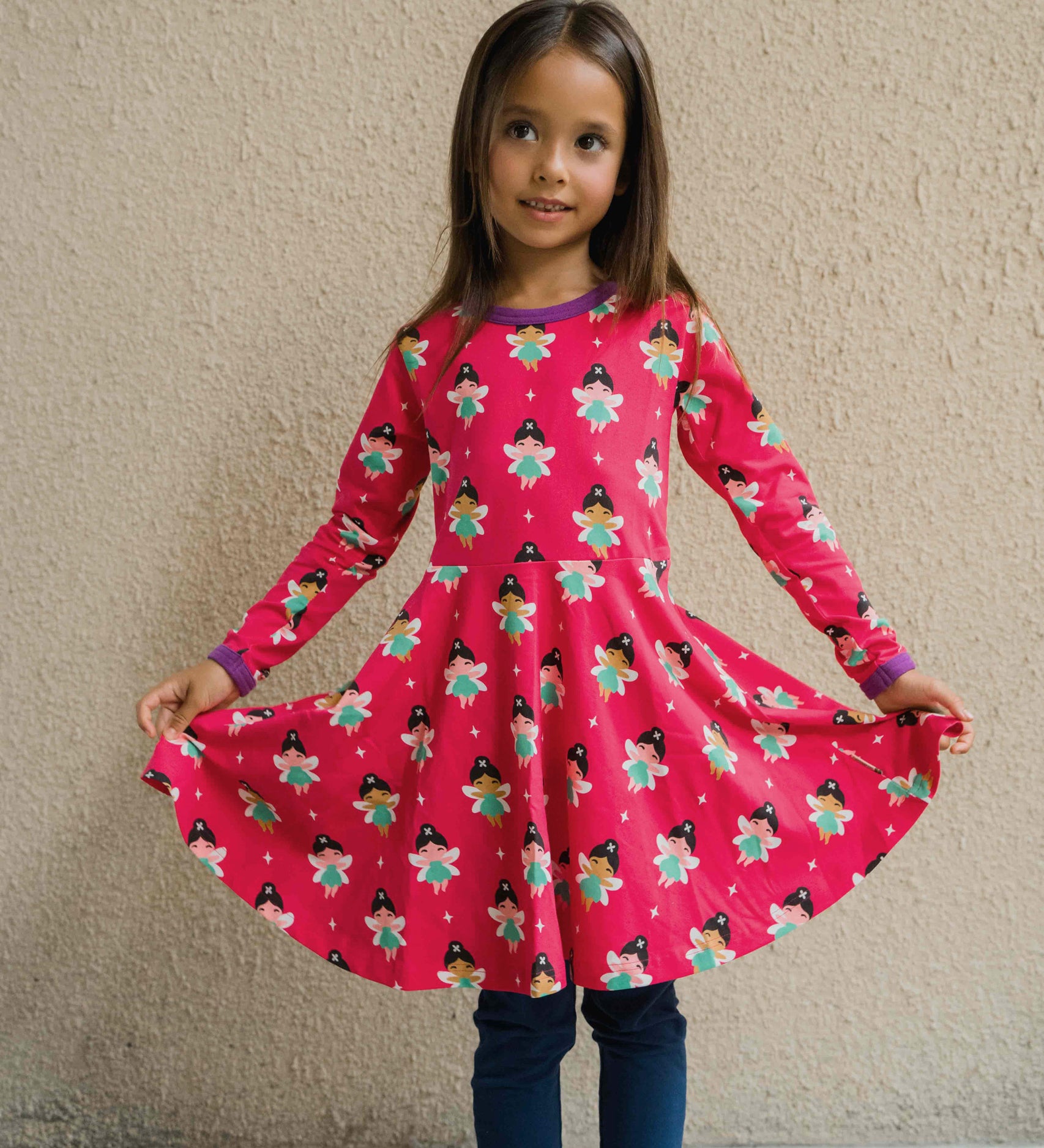 A child wearing the Maxomorra Fairy print circle dress. The child is holding up the sides of the skirt to show the shape. 