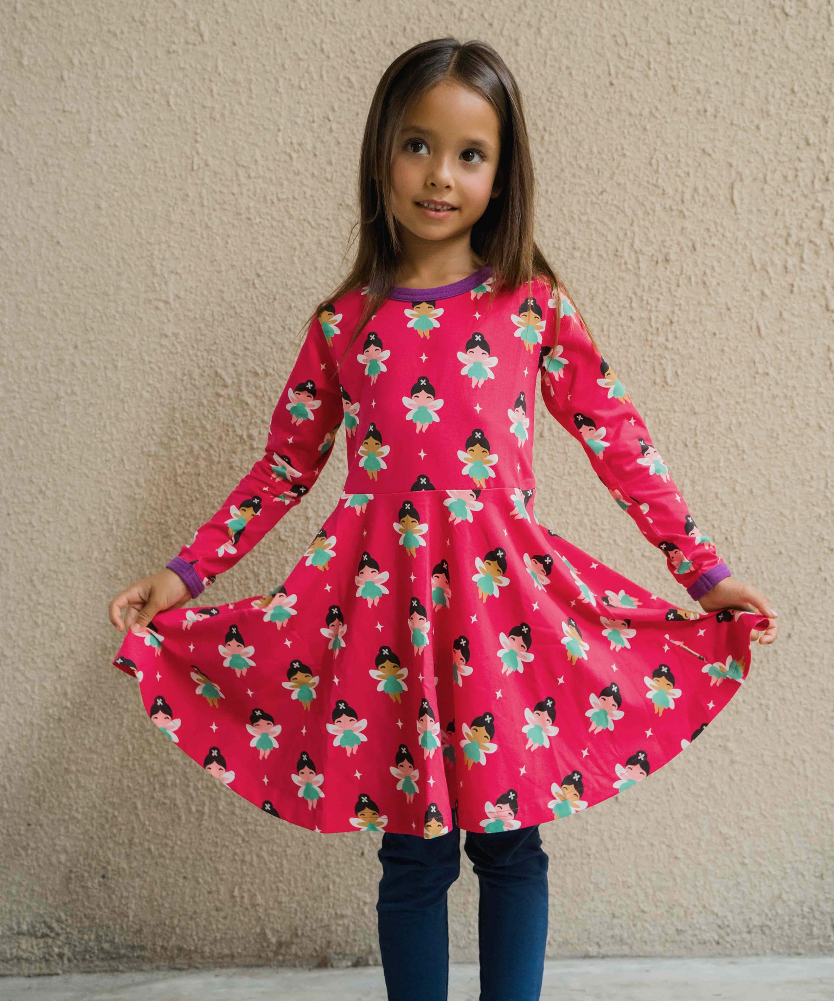 A child wearing the Maxomorra Fairy print circle dress. The child is holding up the sides of the skirt to show the shape. 