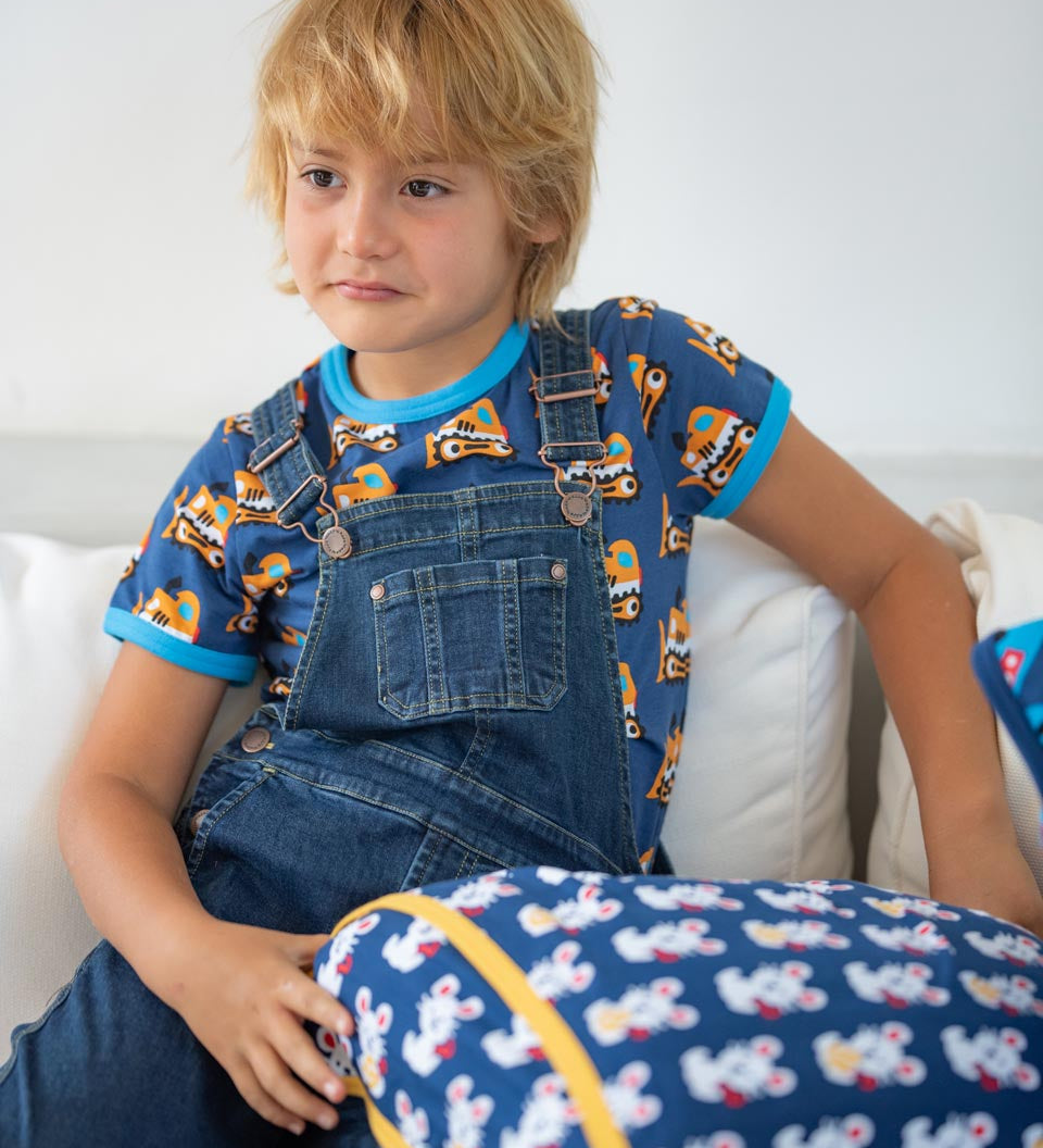 Young boy sat on a white sofa wearing the Maxomorra eco-friendly navy denim dungarees