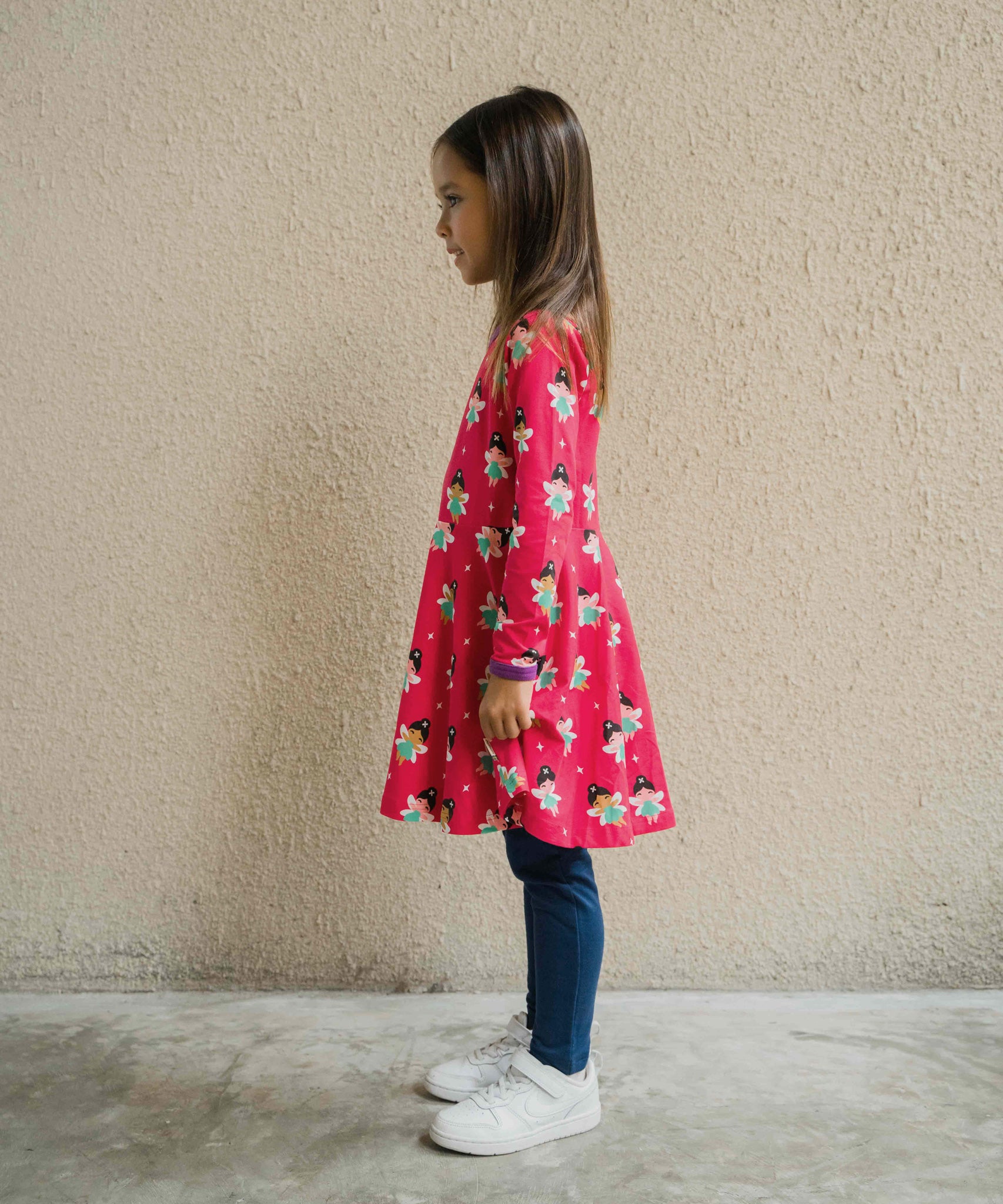 A child wearing the Maxomorra Fairy print circle dress. The child is facing the side showing the side of the dress. 