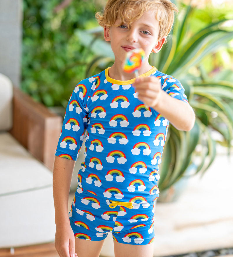 child holding a lollipop wearing the Maxomorra Rainbow Swim Trunks with matching swim top