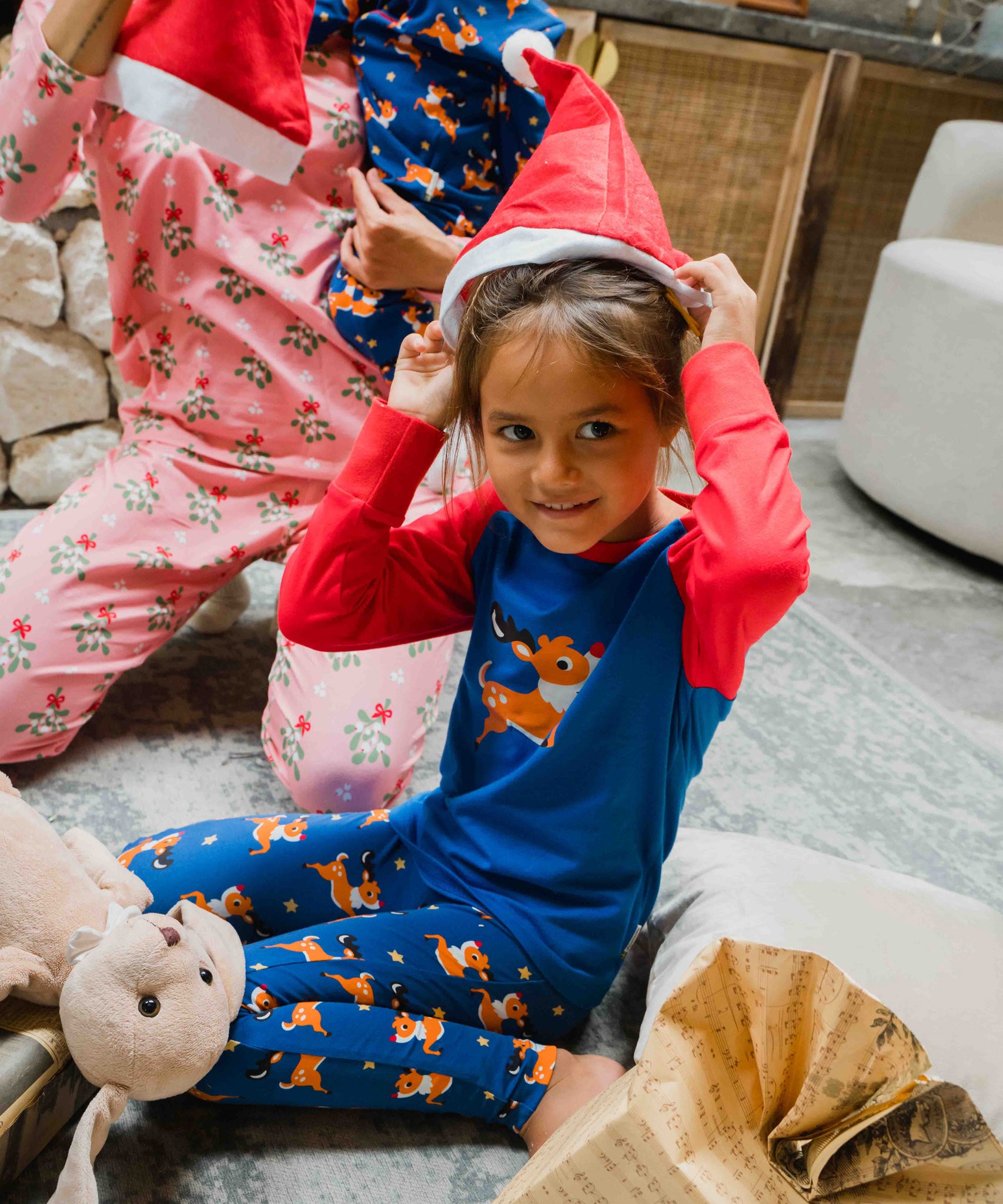 A child wearing the Maxomorra Reindeer Leggings with a coordinating reindeer print raglan top. The child is putting on a red Santa hat.